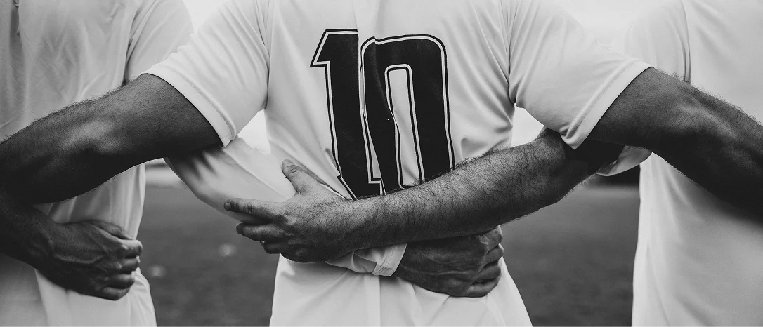 Trois footballeurs en maillot se tiennent bras dessus bras dessous en signe de solidarité, l'accent étant mis sur le maillot numéro 10. La scène incarne l'unité et l'esprit d'équipe